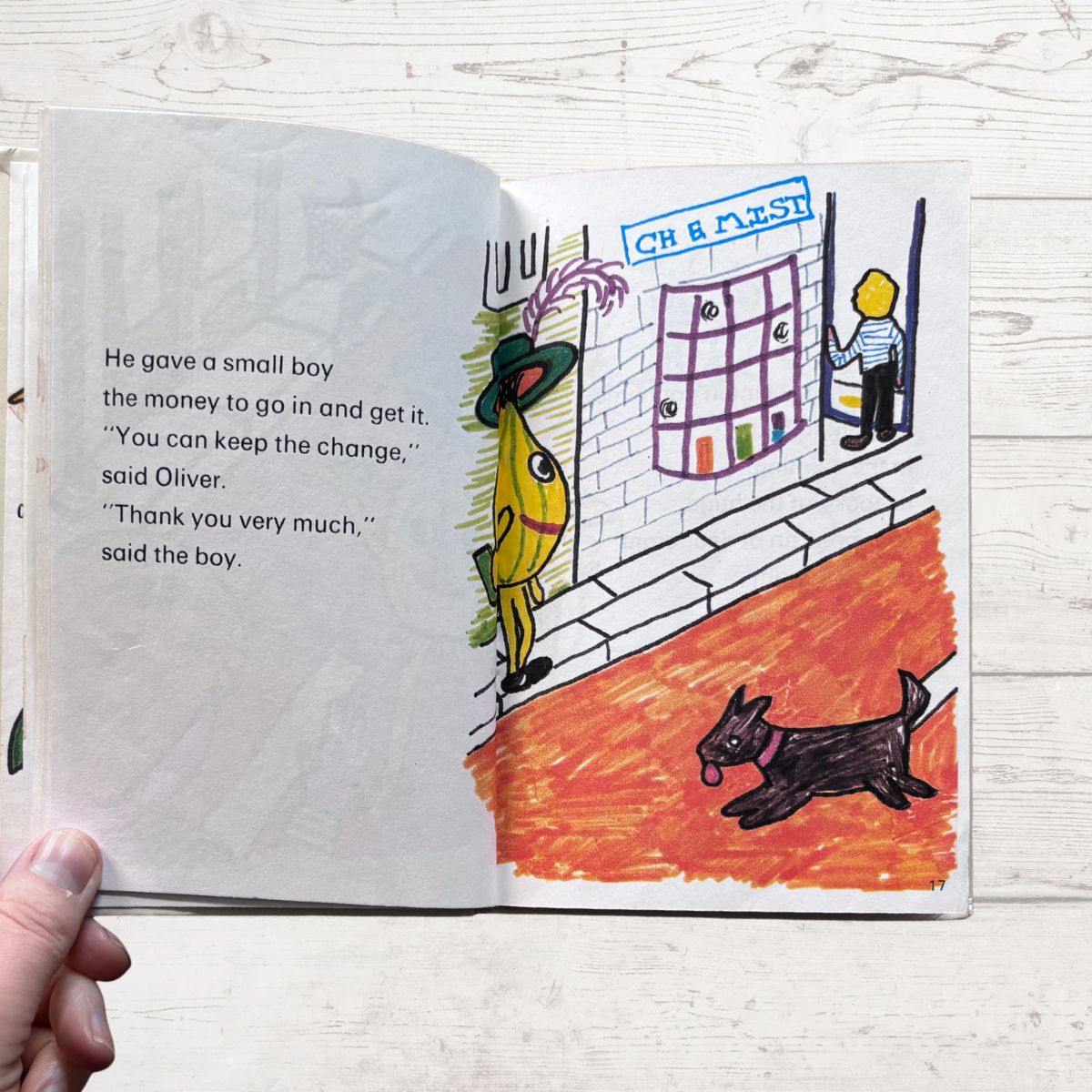 Open book with illustrated page showing a scene with a boy, dog, and colorful characters on a wooden surface.