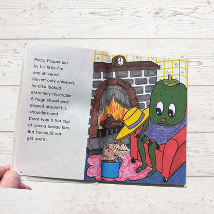 Illustrated book page with a character by a fireplace, on a wooden surface.