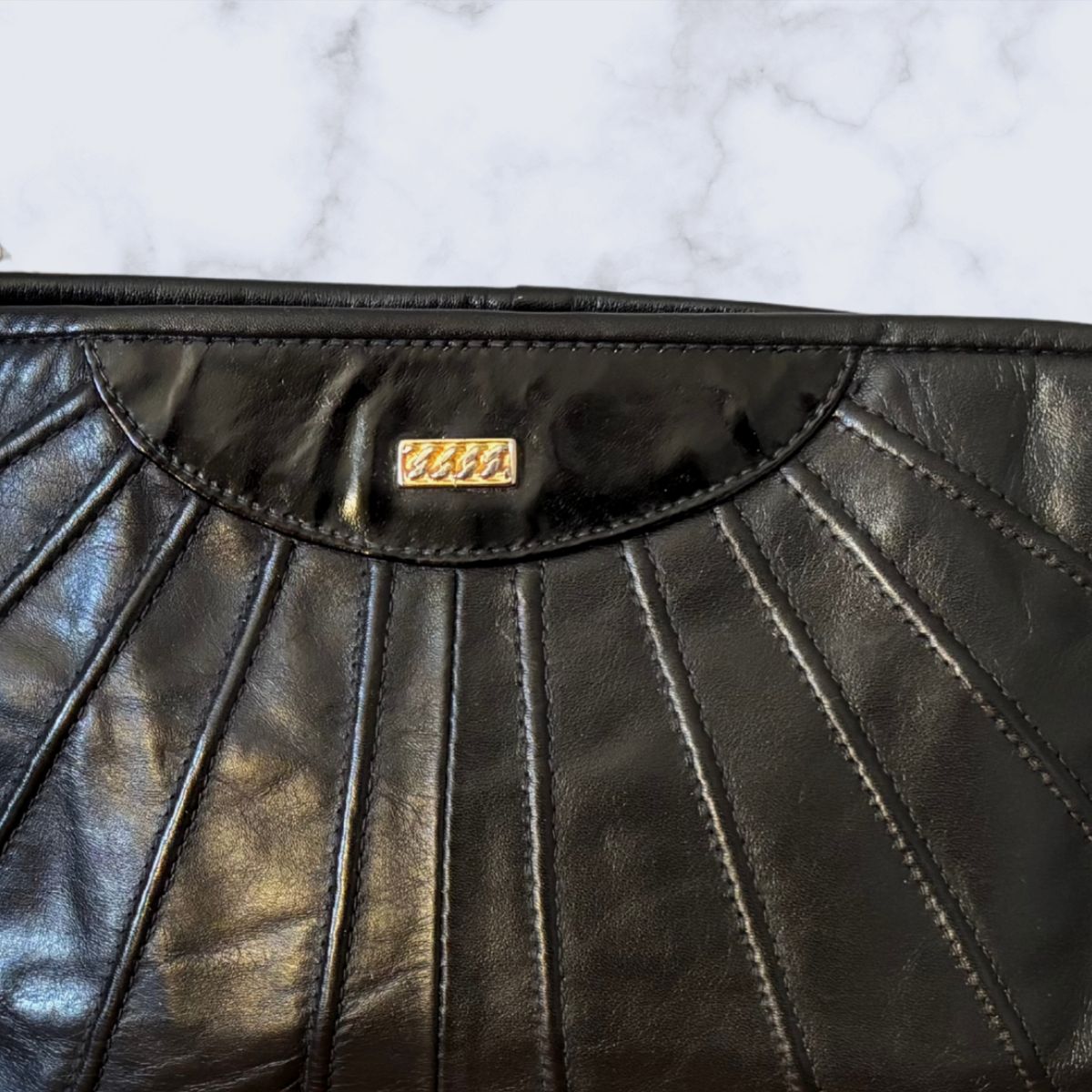 Black leather handbag with a visible gold chain  logo on a white marble surface