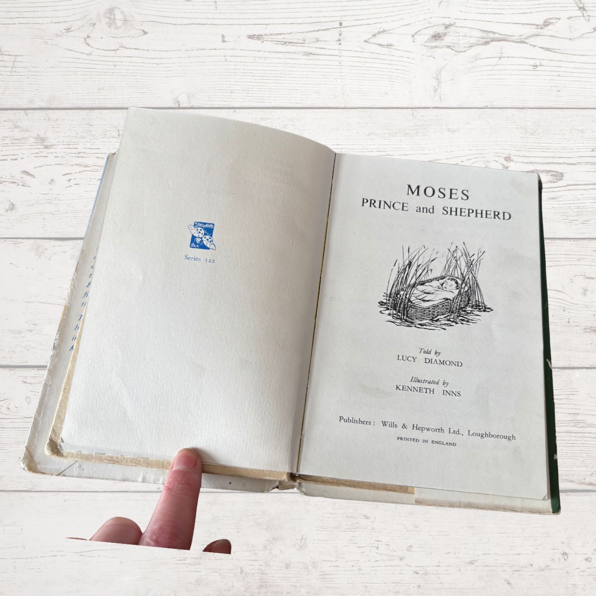 Open book titled 'Moses Prince and Shepherd' held by a hand on a light wooden surface.