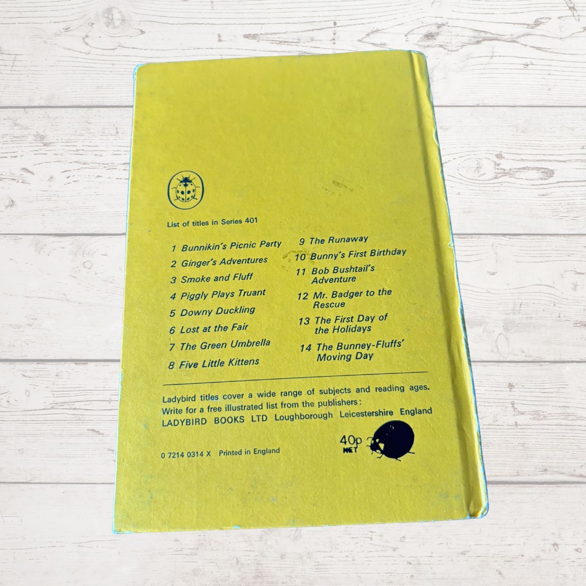 A yellow-green hardcover book lying flat on a white wood-textured surface, showing the back cover with a printed tracklist, publisher details for Ladybird Books, and a black circular stamp.