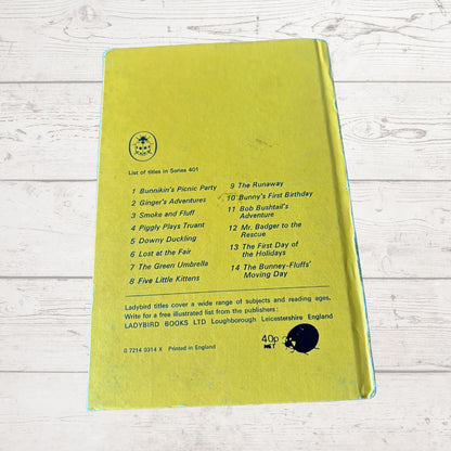 A yellow-green hardcover book lying flat on a white wood-textured surface, showing the back cover with a printed tracklist, publisher details for Ladybird Books, and a black circular stamp.