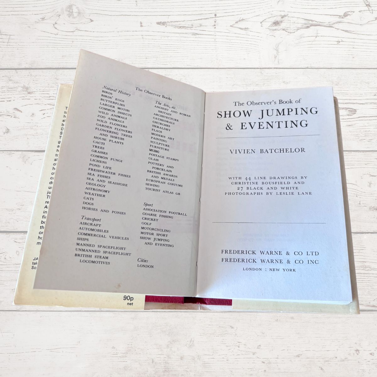 An open vintage book titled 'The Observer's Book of Show Jumping & Eventing' by Vivien Batchelor, displayed on a light whitewashed wooden surface. The left page shows a list of jumpers, and the right page displays the title page with publisher details for Frederick Warne & Co Ltd.