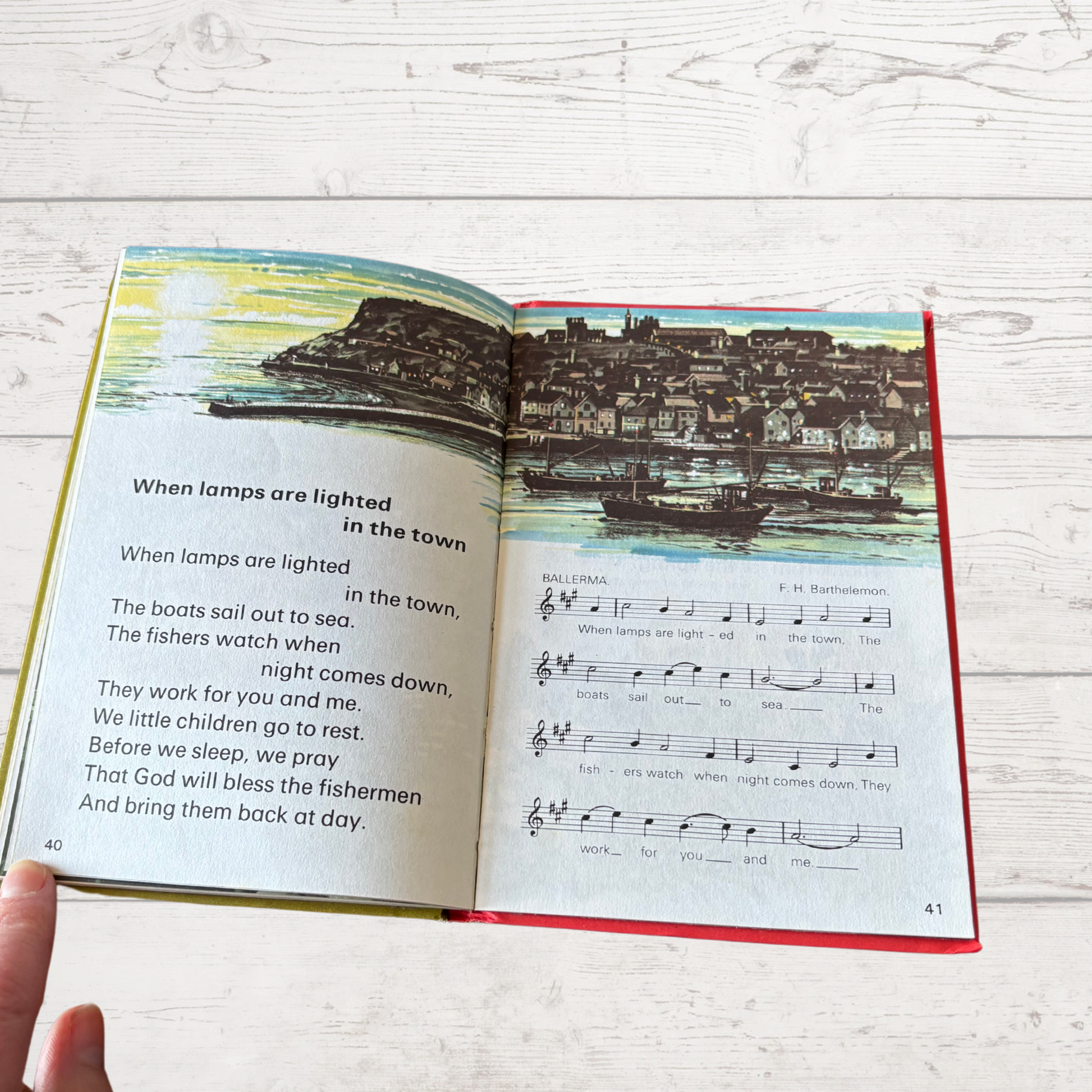 Open book with a colorful illustration of a town by a body of water on a wooden surface.
