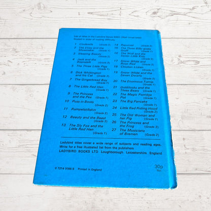 A blue back cover of a Ladybird Books children's book lies flat on a white-washed wooden surface. The cover features a black printed tracklist of 25 animal stories with level headings from Grade 1 to Grade 3.