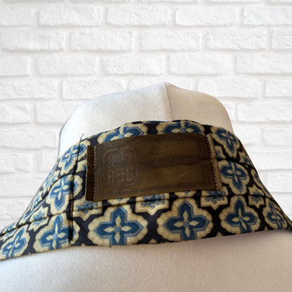 A vintage Austin Reed labelled cravat featuring a black necktie with a cream, gold, and blue stylized floral print, displayed on a mannequin against a white brick wall background.
