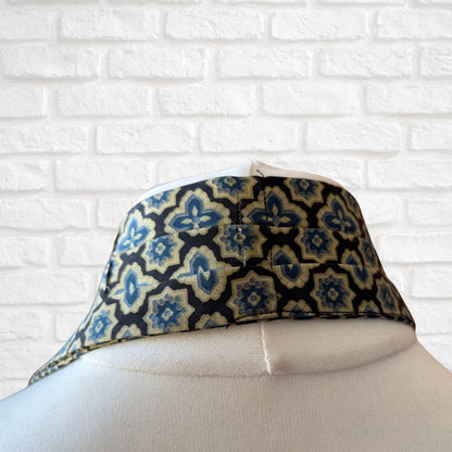 Pleated back of vintage Austin Reed cravat featuring a black necktie with a cream, gold, and blue stylized floral print, displayed on a mannequin against a white brick wall background.