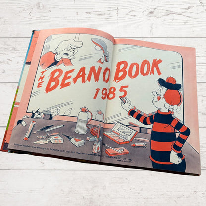 Open book titled 'The Beano Book 1985' on a wooden surface