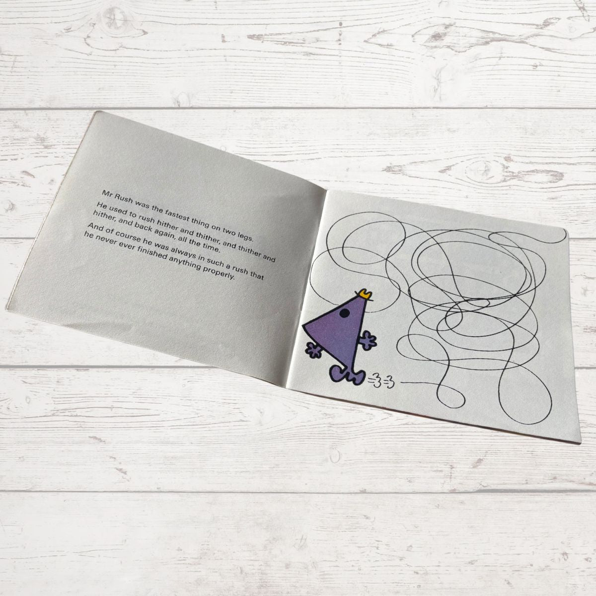 Open book with a drawing of a purple triangle character and text on a wooden surface