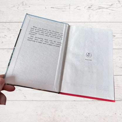 An open hardcover book with printed text on the left page and a blank page on the right, held by a hand against a light wood plank background.
