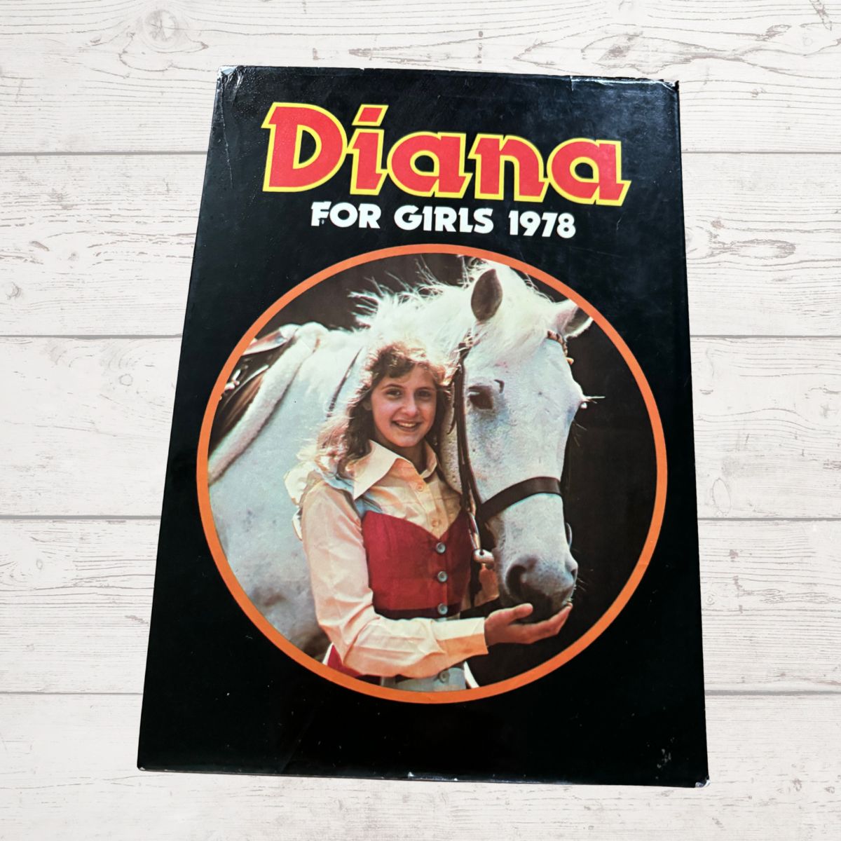 Book titled 'Diana for Girls 1978' featuring a girl and horse on the cover, placed on a wooden surface.