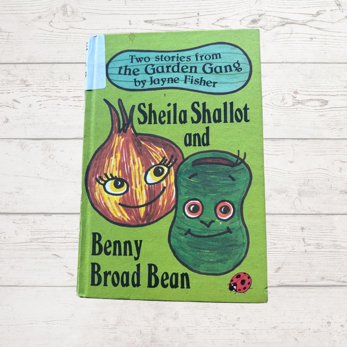 Book cover of 'Sheila Shallot and Benny Broad Bean' by Jayne Fisher on a wooden surface