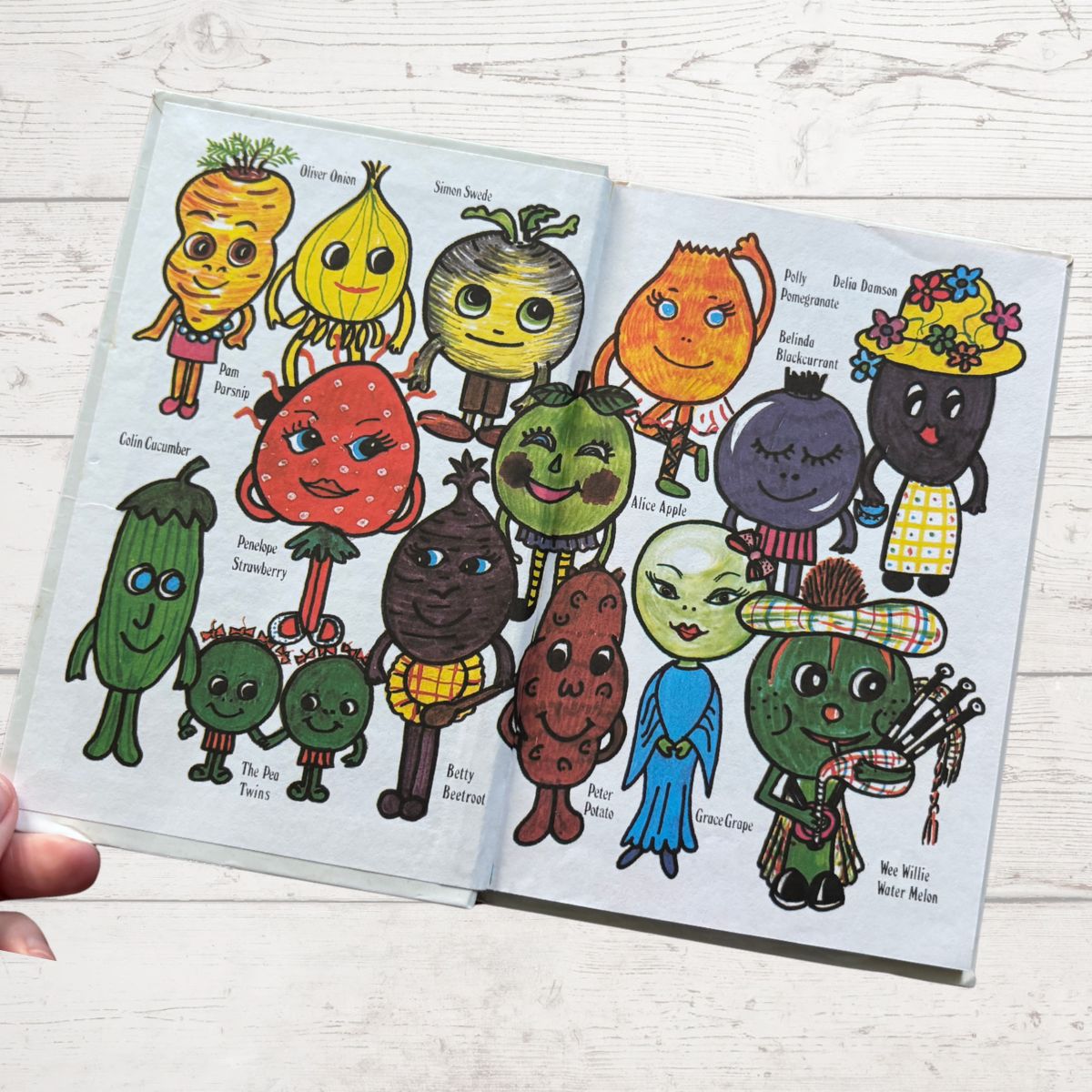Colorful illustrated book open to pages with character illustrations on a white wooden surface.