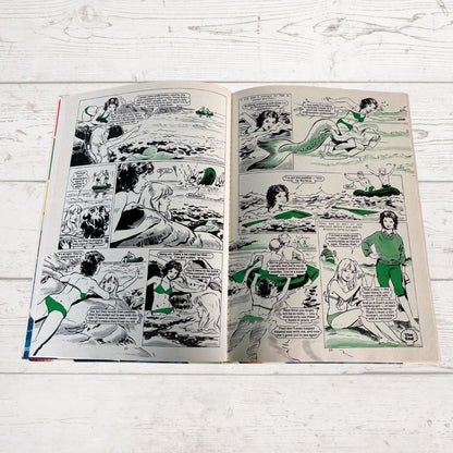 Comic book open to a page with multiple panels on a light wooden surface