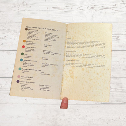 An open vintage book showing printed text and colored title labels on aged cream paper, photographed on a white wood surface. 