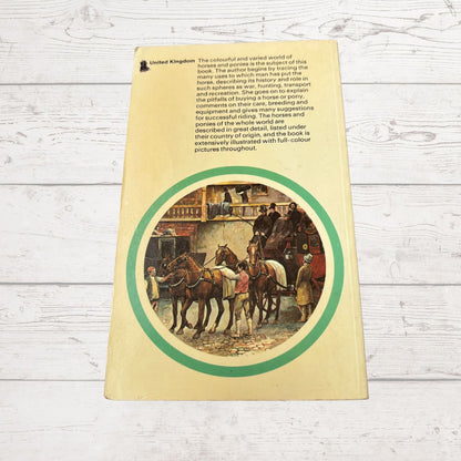 The back cover of a vintage book titled 'United Kingdom' lies flat on a white wood-plank surface. The cover is cream-colored with black descriptive text at the top and a large circular vintage illustration featuring horses and people inside a green oval border.
