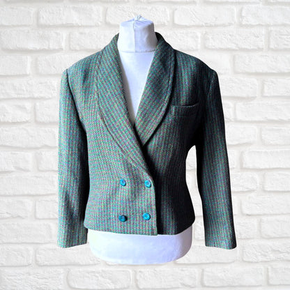 A women's double-breasted blazer in a green and blue herringbone tweed pattern, styled on a white mannequin torso against a white brick wall background.