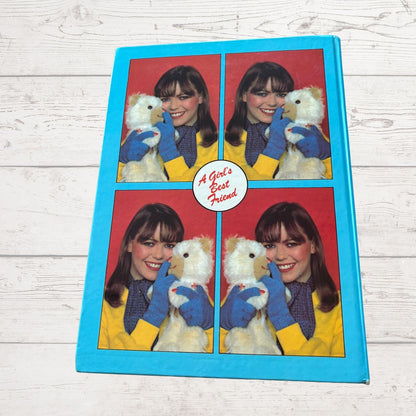 Book with a design of a person holding a teddy bear, surrounded by text 'A Girl's Best Friend' on a wooden surface.