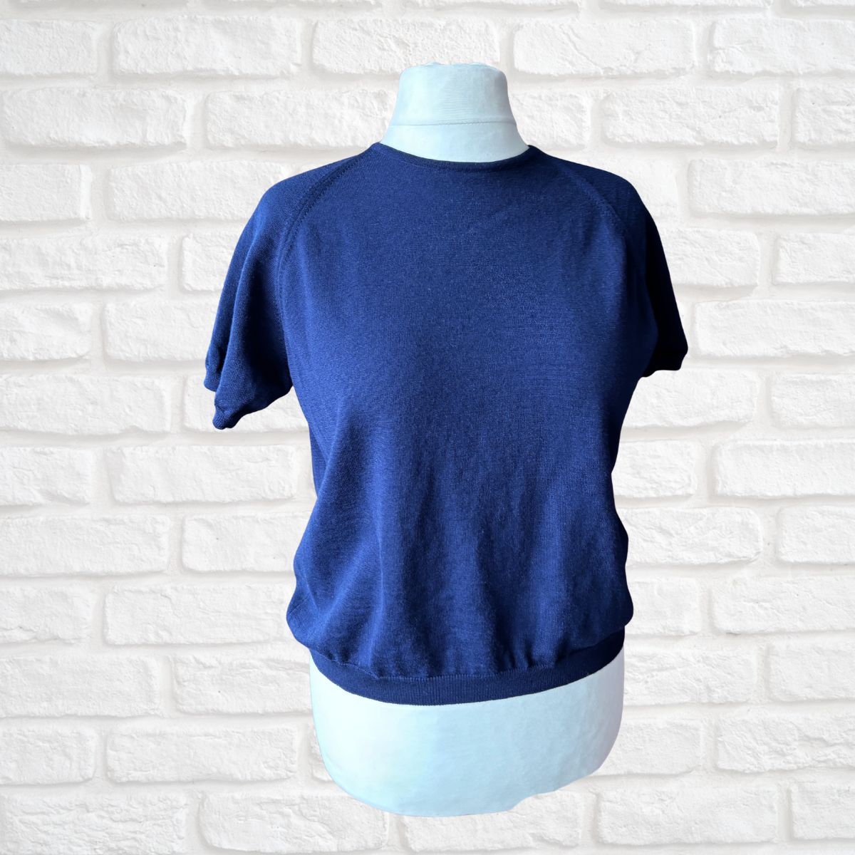 Blue sleeveless top on a mannequin against a white brick wall background