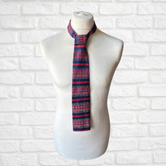 Mannequin wearing a red and blue patterned tie against a white brick wall.