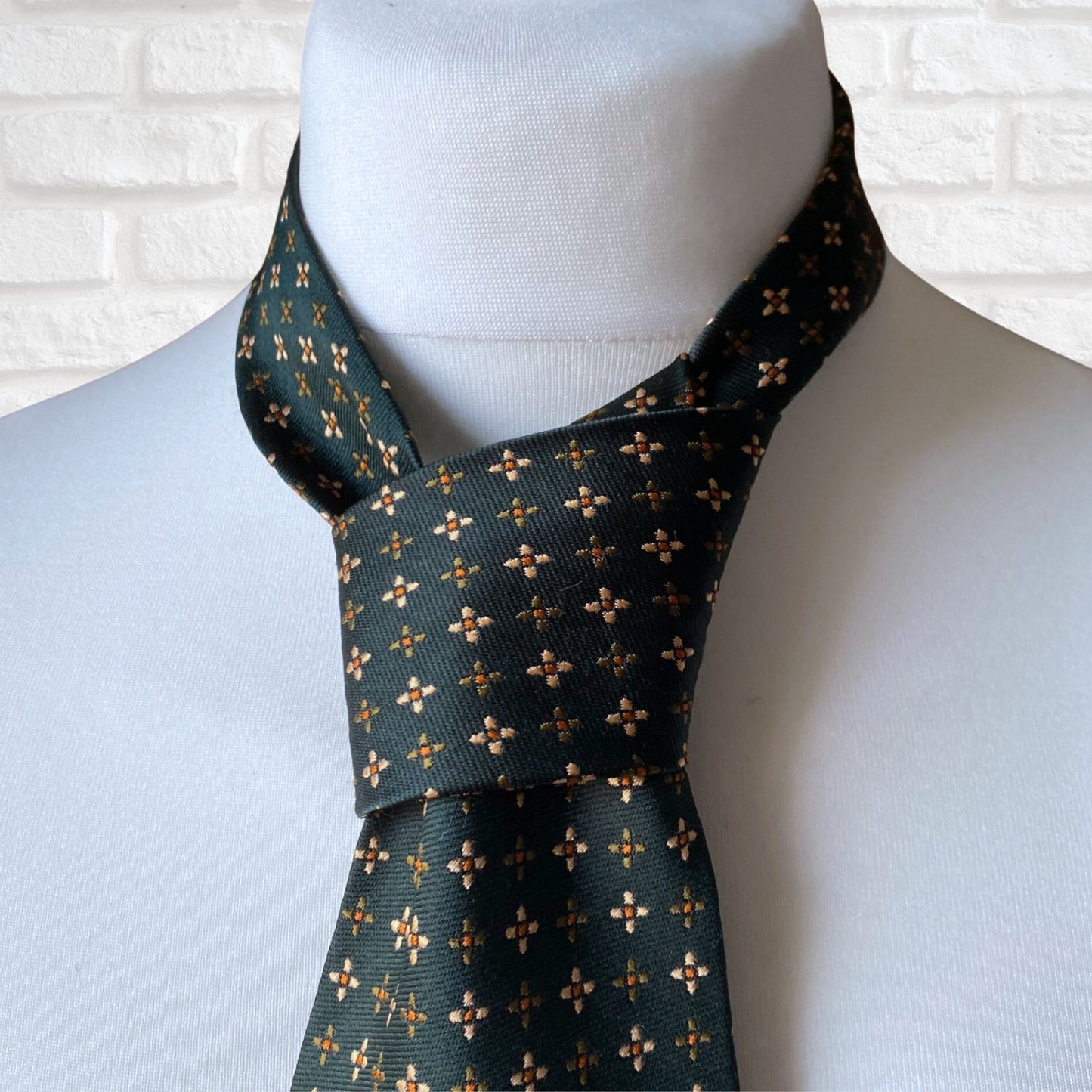 Close up of a green, orange and white geometric floral  print vintage 70s tie on a mannequin.
