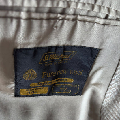 Close-up of a garment's interior label reading 'St. Michael's' and 'Pure new wool' in gold embroidery on a dark navy patch, with light beige fabric surrounding it.