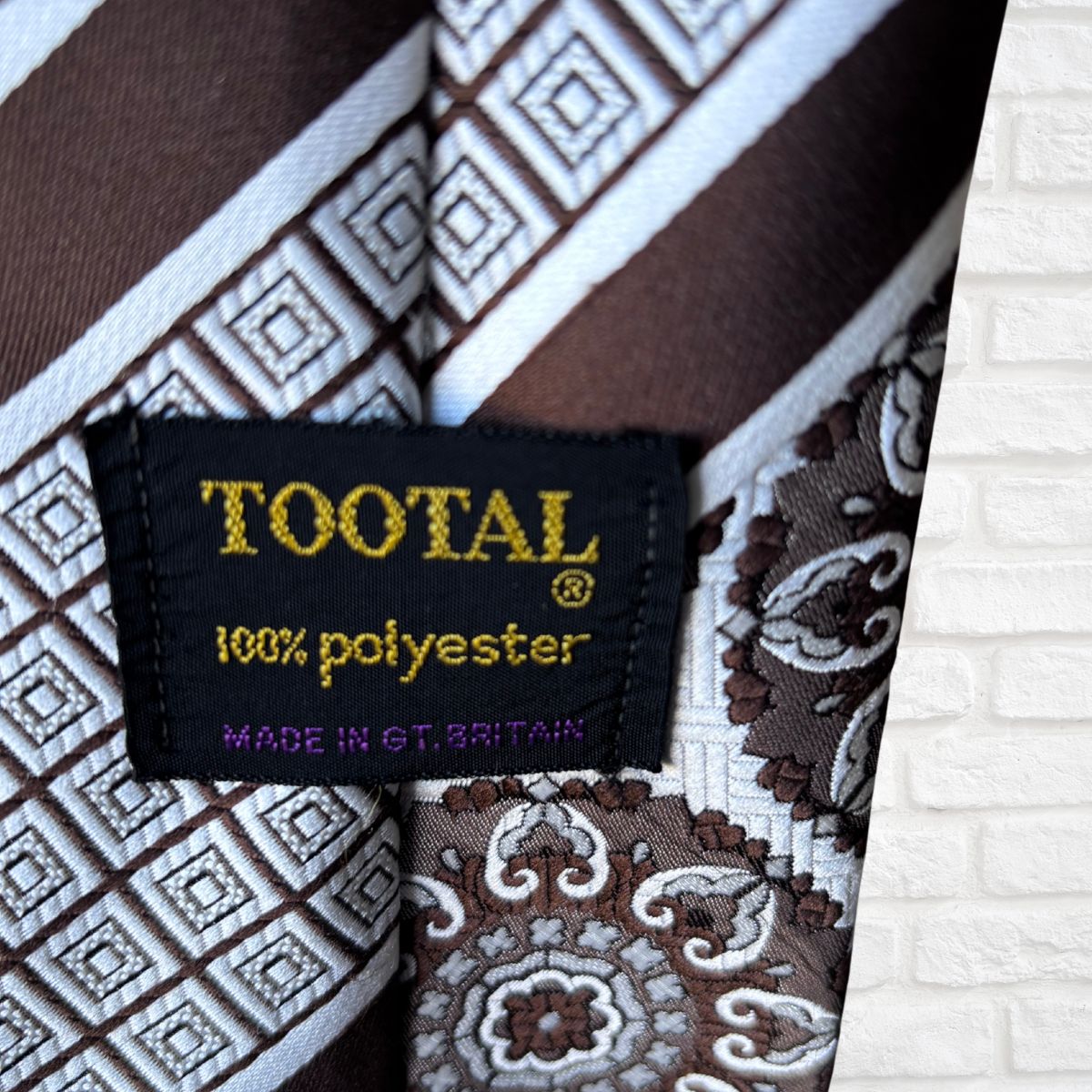 Close-up of a patterned tie with a Tootal label on a white brick wall background