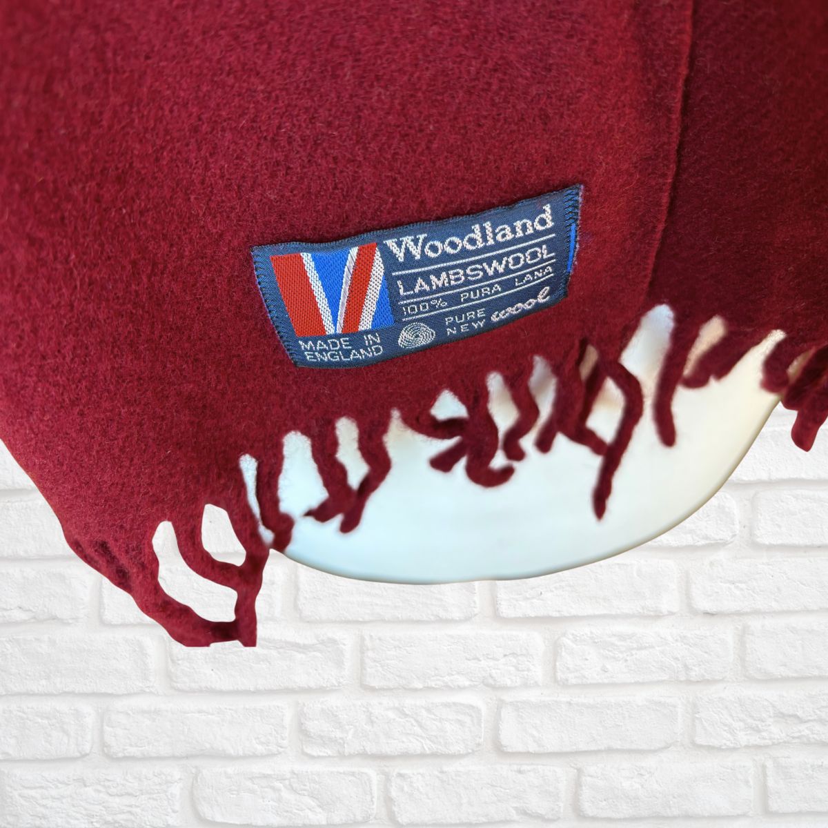 Red scarf with a 'Woodland Lambswool' label on a white brick background