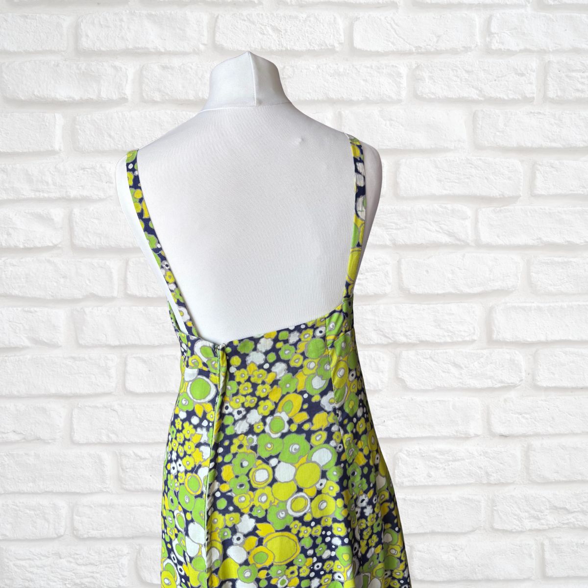 Mannequin wearing a floral dress against a white brick wall.