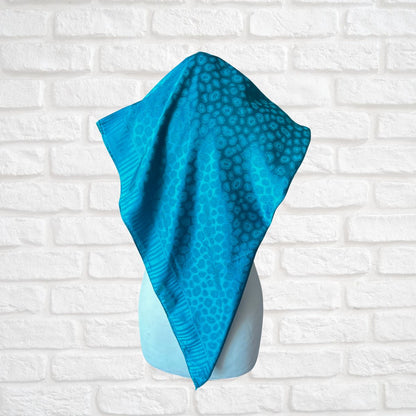 Blue textured scarf on a mannequin against a white brick wall background