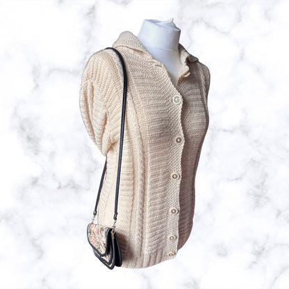 A cream-colored, textured knit cardigan sweater displayed on a white mannequin torso, styled with a small black shoulder bag against a white marble background.