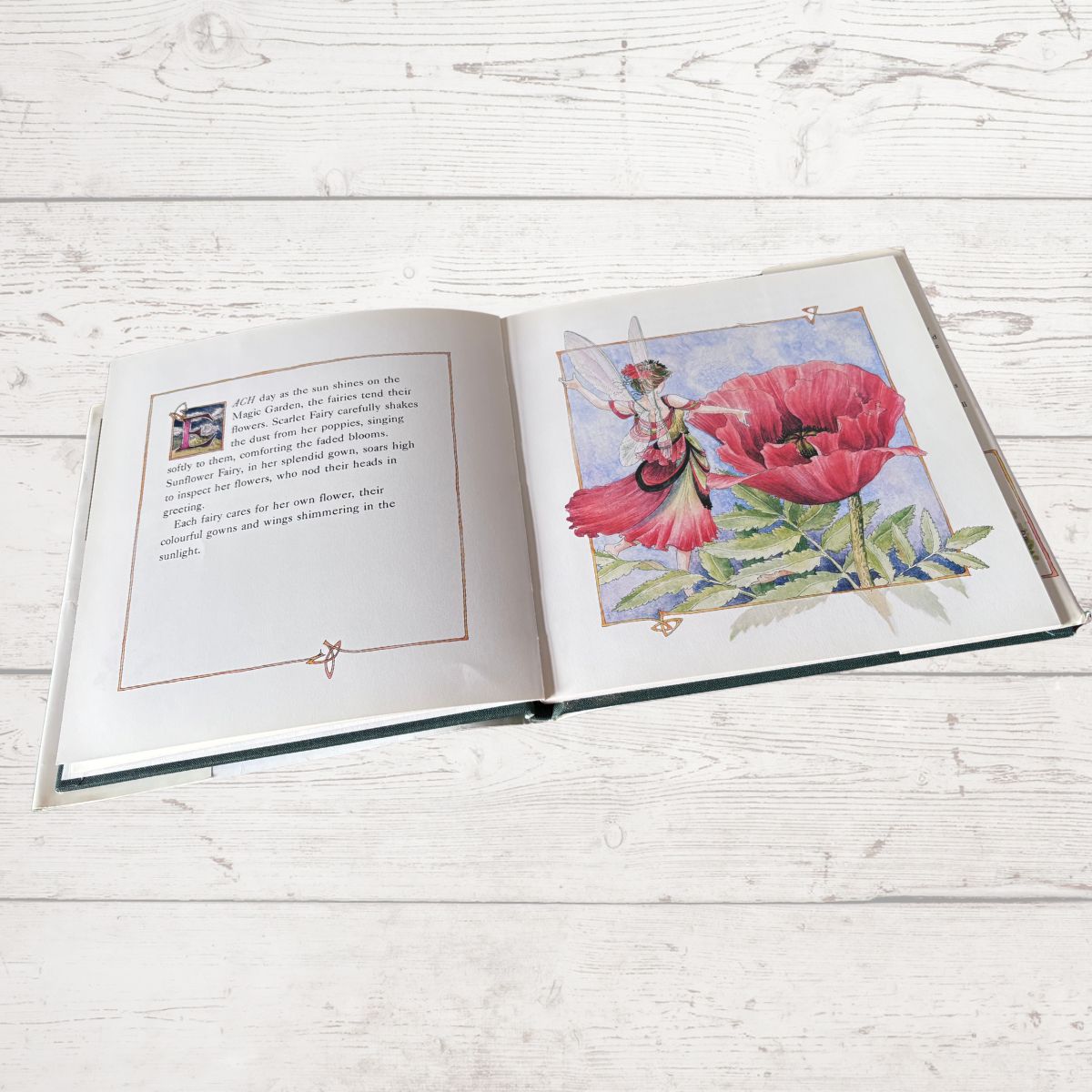 Open book with illustrations of a fairy and a pink flower on a wooden surface