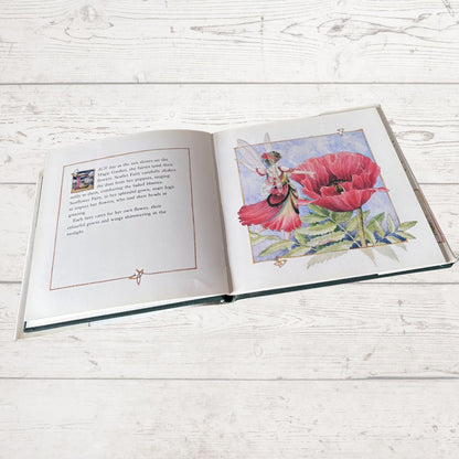 Open book with illustrations of a fairy and a pink flower on a wooden surface