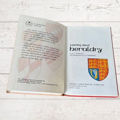 Open book on a wooden surface with text and a coat of arms illustration.