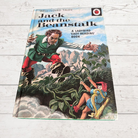 Vintage paperback book of Jack and the Beanstalk lying on a white wood-plank surface. The cover shows a colorful illustration of a man climbing a giant beanstalk toward a person in a blue dress.