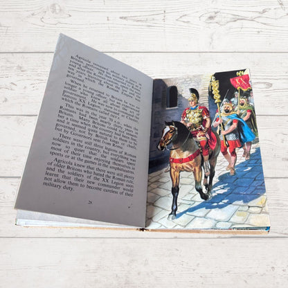 An open book lying on a white wooden surface, showing printed text on one page and a colorful illustration on the other of soldiers on horseback in historical dress.