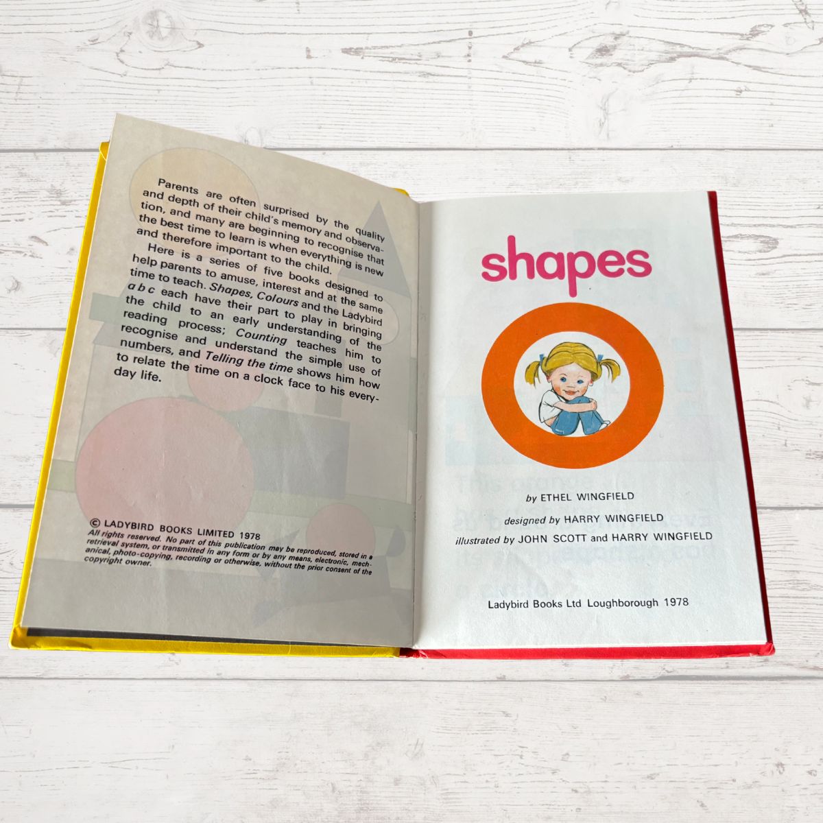 Open book showing a page titled 'shapes' with a child illustration on a light wooden surface.