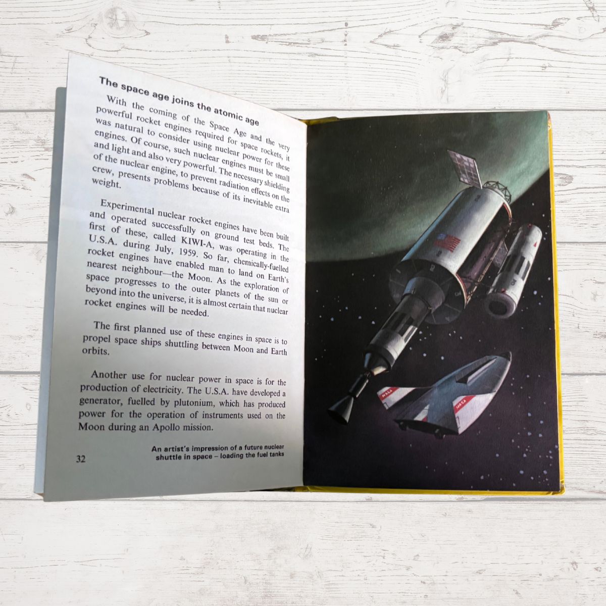 An open children's book showing a space-themed page with text on the left and an illustration of a rocket ship in orbit on the right, placed on a white wood surface.