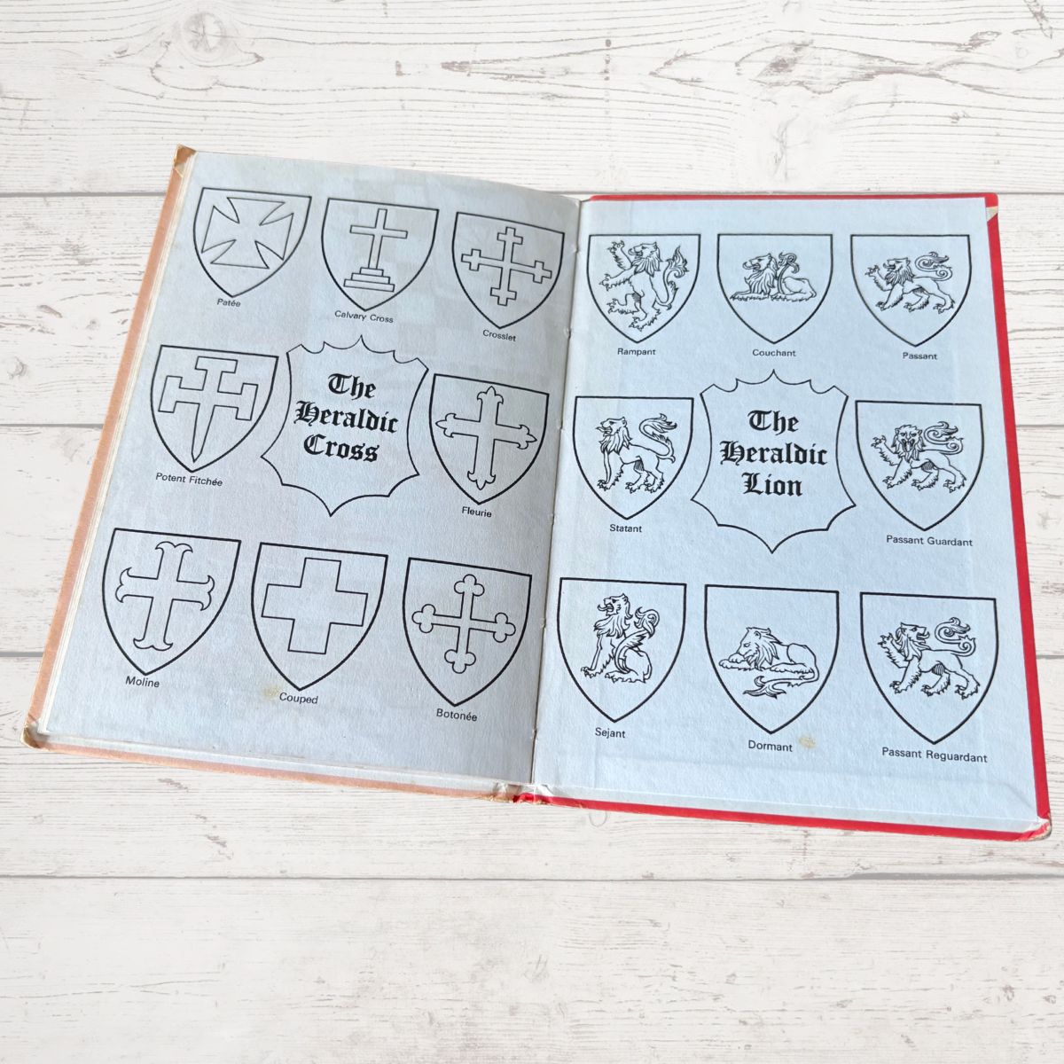 Open book with pages displaying heraldic symbols on a wooden surface