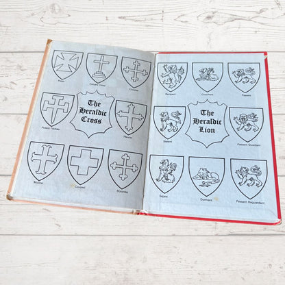 Open book with pages displaying heraldic symbols on a wooden surface