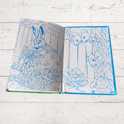 An open book featuring blue line art illustrations of rabbits and garden scenes on cream-colored pages, placed on a white wooden surface.