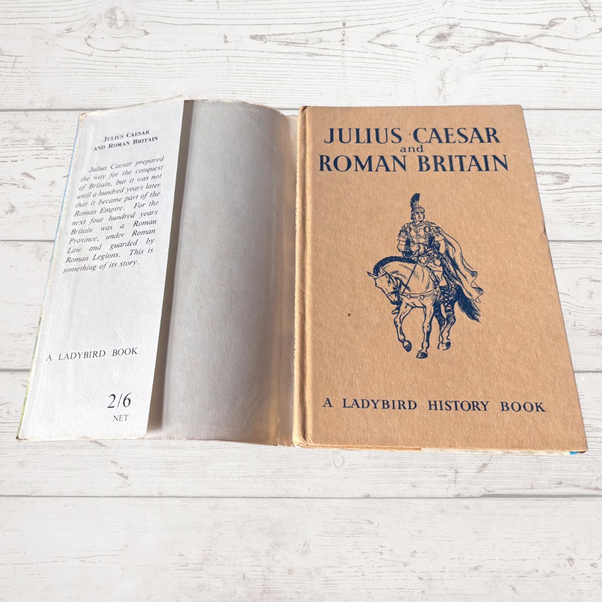 An open vintage book titled 'Julius Caesar and Roman Britain' by A. Ladybird, showing the tan cover with a dark blue illustration of a Roman soldier on horseback and the white interior pages.