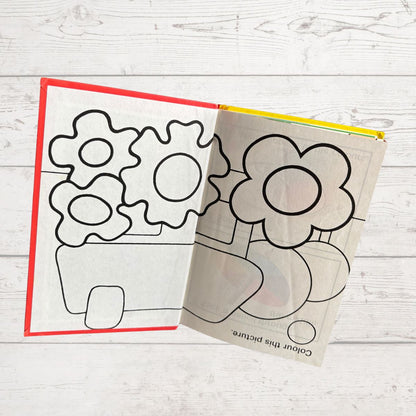 Coloring book with flower and gear designs on a wooden surface