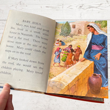 Open book with a story about Baby Jesus and Mary, held by a hand on a light wooden surface.