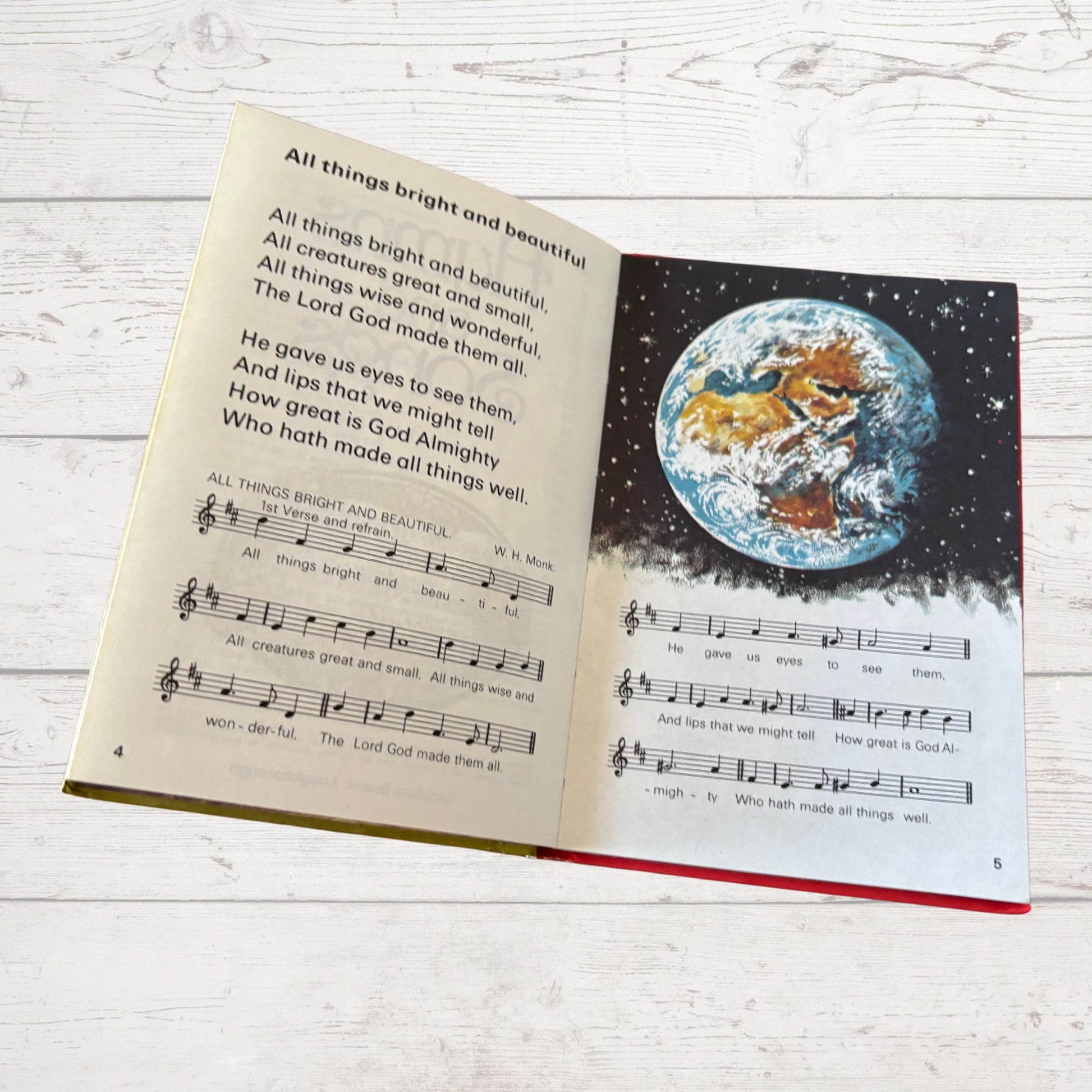 Open book with lyrics and a world illustration on a white wooden surface