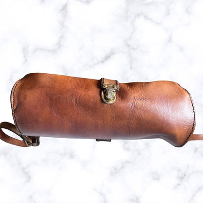 A brown leather handbag with a brass-tone clasp closure, photographed horizontally against a white marble-patterned background.