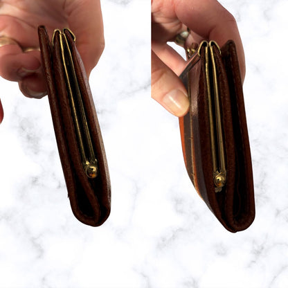 Two hands holding a brown leather wallet with gold accents against a white background