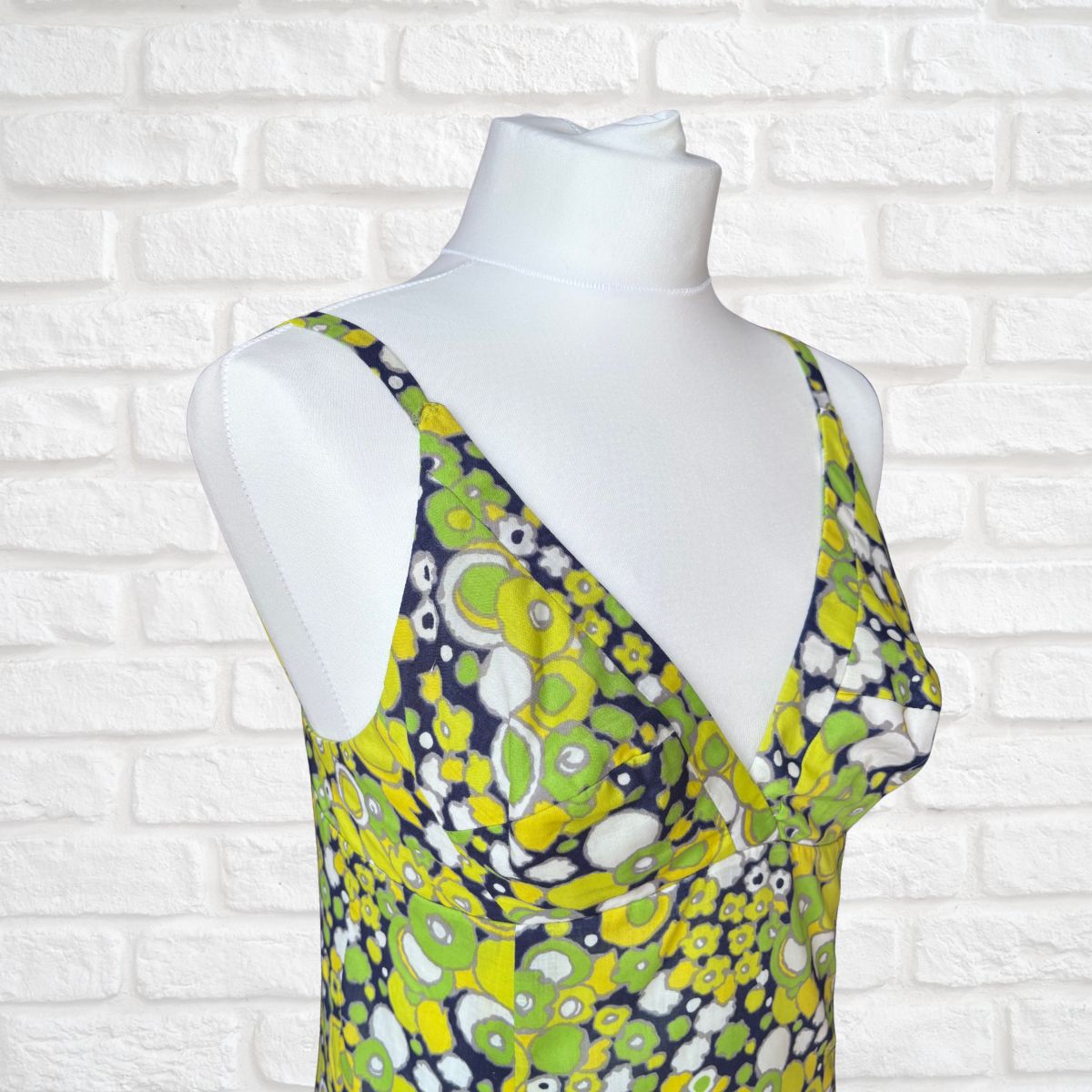 Mannequin wearing a geometric floral dress against a white brick wall.