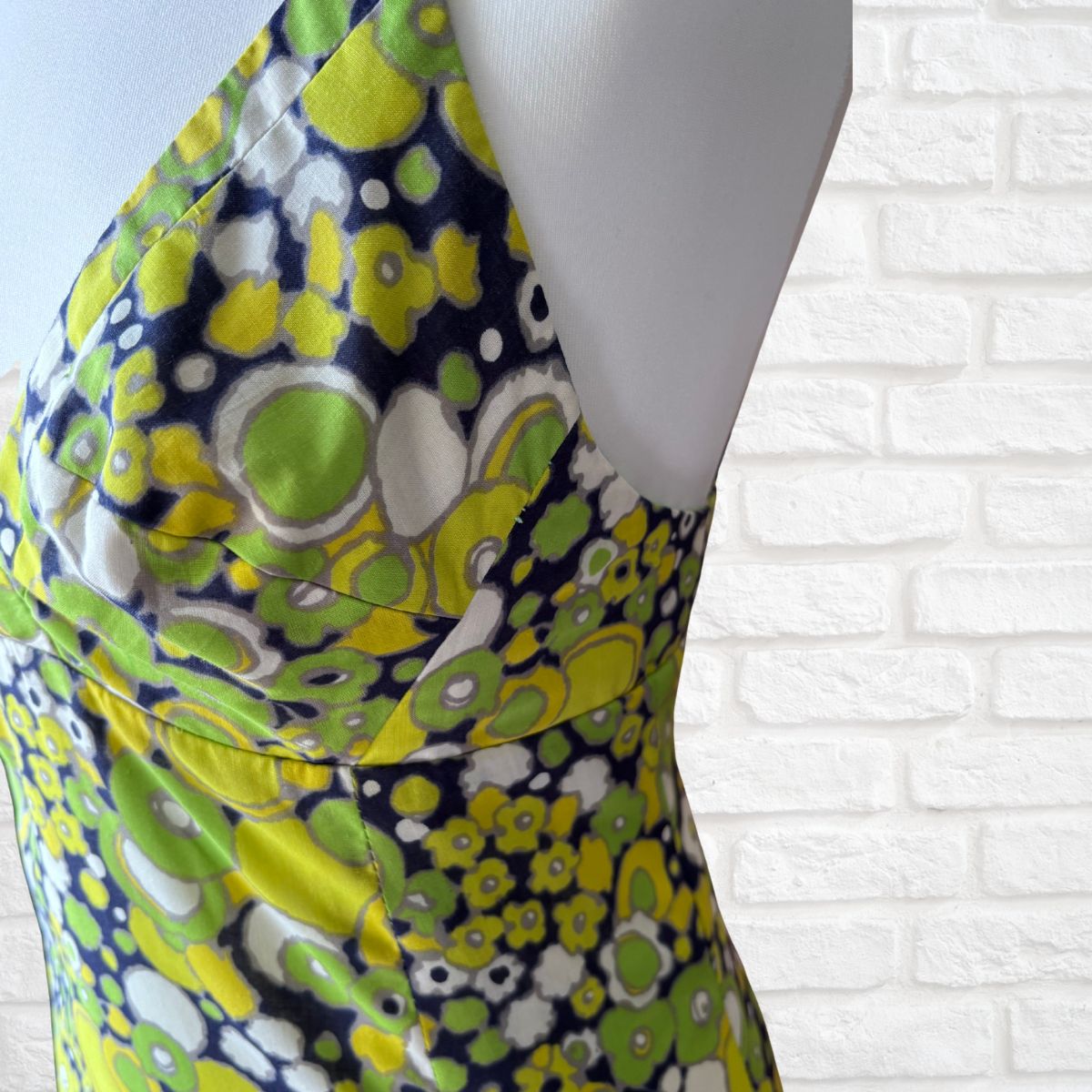 Mannequin wearing a colorful floral-patterned dress against a white brick wall.