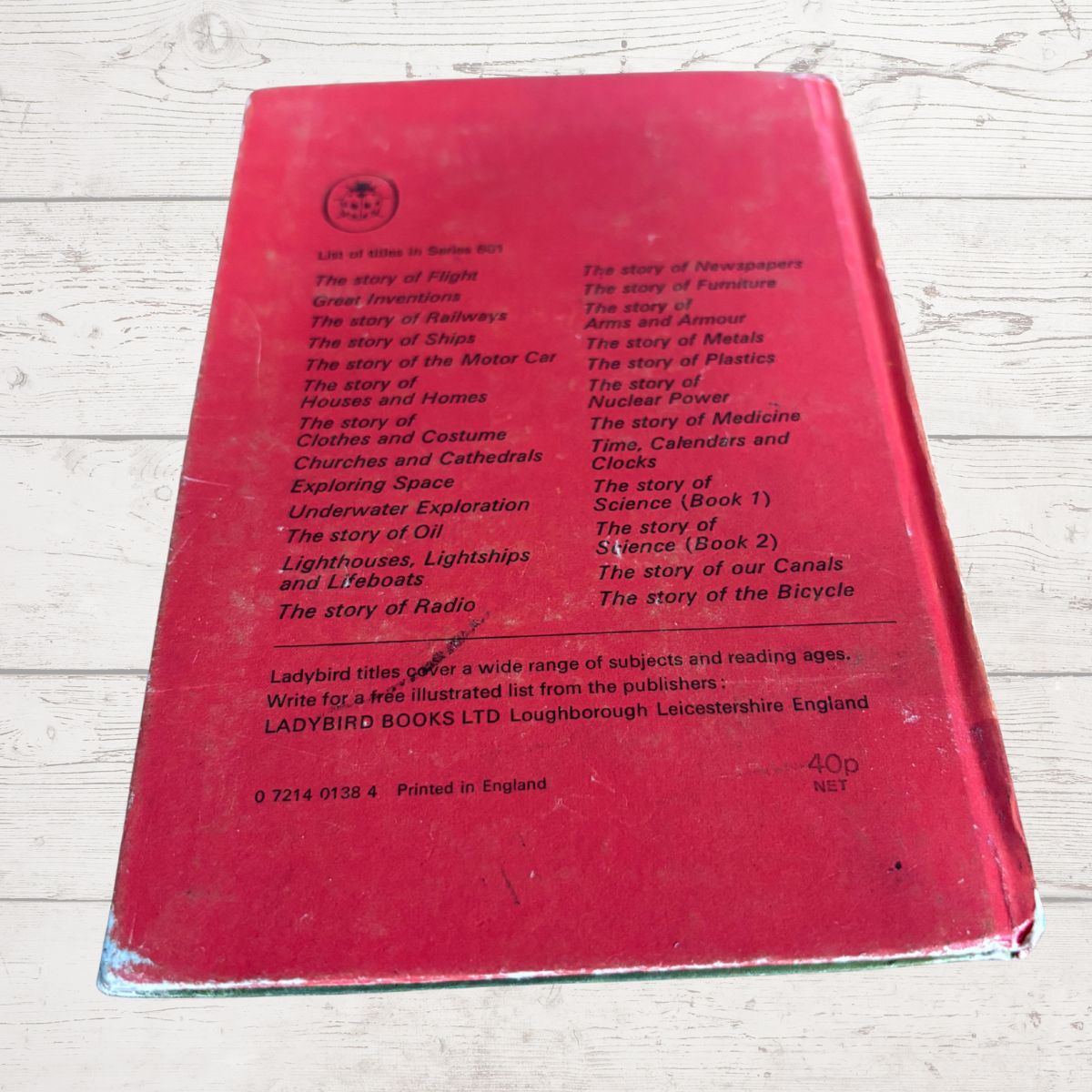 A vintage red Ladybird book, likely from the 1960s, photographed from above on a light-colored wooden surface. The back cover features printed red text listing various educational and general knowledge topics under the Ladybird title format.